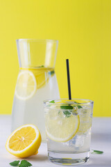 glass of lemonade.Summer refreshing cocktail with lime and mint on white and yellow background. Fresh summertime iced drink with yellow citrus and green leaves in glass and jug. copy space. vertical