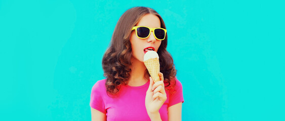Portrait of happy young woman eating ice cream wearing summer sunglasses on blue background
