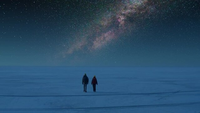 The two tourists walking through the snow field on the starry sky background

