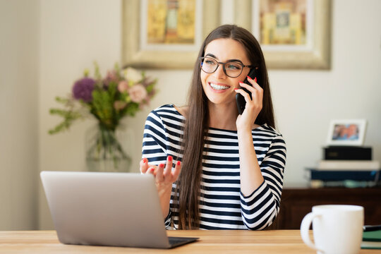 Attractive young woman using laptop and mobile phone while sitting at desk at home