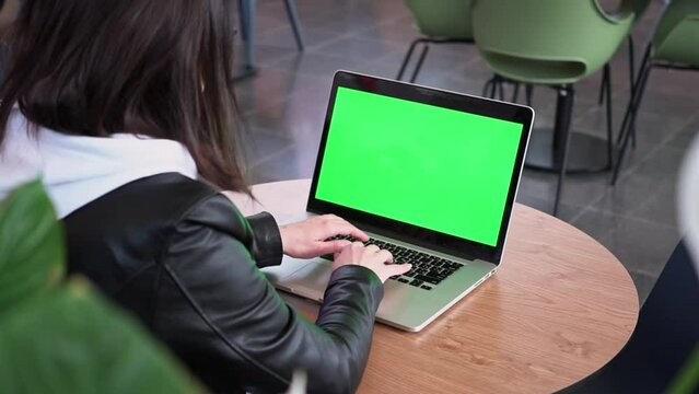 Shot over shoulder Caucasian business woman working in an office interior at computer on desk, looking at green screen. Office man using green screen laptop computer while sitting at wooden table