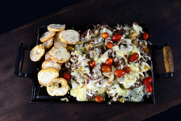 roast beef on iron plate with cheese, tomato pepper herbs, onion, cassava and bread