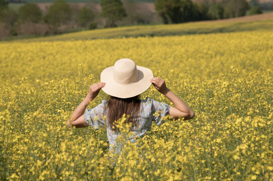 Woman In A Field Of Yellow Wild Flowers Holding Her Sun Hat In Summer