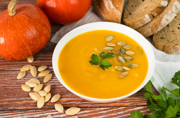 Cream of pumpkin soup and freshly baked hot bread on a wooden table. Close-up.