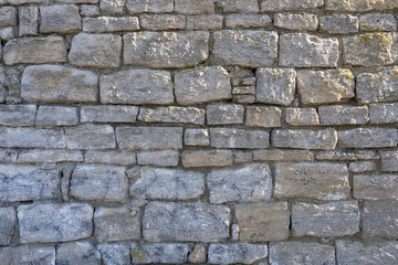 Fragment of an old fortress wall made of gray limestone. The right corner is slightly lit by the rays of the sun. Background. Texture.