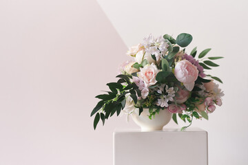 A composition of different flowers in a white vase on a square podium. The concept of a flower shop. A beautiful freshly cut bouquet. Flower delivery. High quality photo