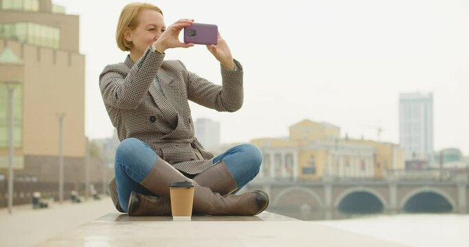 40-year-old beautiful woman taking a photo of cityskape with her smartphone during coffee break.