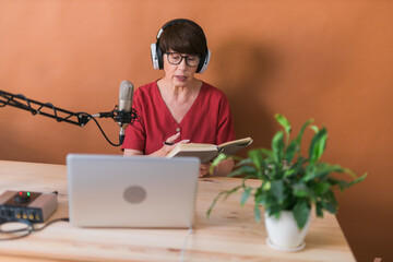 Portrait of mature woman wearing headphones and talking at online radio station - podcast and...