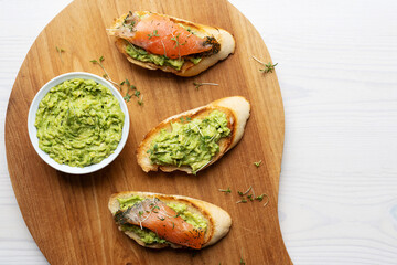 Toasted bread with guacamole and salmon slices, bowl with avocado cream.