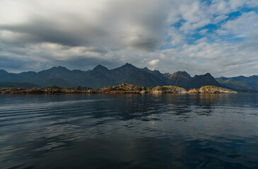 Norwegian seascape, rocky coast with dramatic skies, the sun breaks through the clouds, sheer cliffs, small islands illuminated by the sun