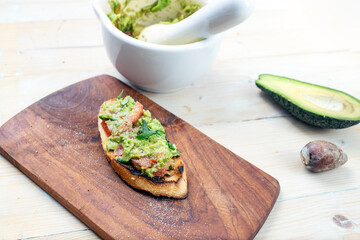 Guacamole on a baguette slice, rustic décor with wood boards and  a mortar and pestle