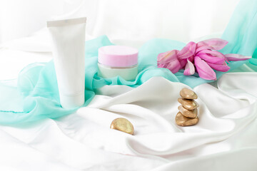 Fototapeta na wymiar tube and jar without label, product mockup for skin care products, with white satin golden zen stones and magnolia flowers