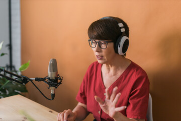 Portrait of mature woman wearing headphones and talking at online radio station - podcast and...