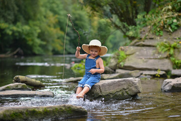 Funny happy little kid fishing at the lake. A fisher boy sits in the lake with a fishing rod and catches fish
