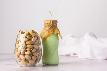 Pistachio milk in a green bottle with a cloth lid, standing beside a jar overflowing with shelled...