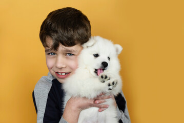 A happy young boy hugs a white dog puppy, the boy is glad that he was given a new friend - a puppy for his birthday. Child and pet friendship concept