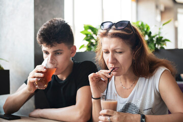 A woman with her teenage son in a cafe drinking juice and not talking yet because they quarreled over the hot-tempered nature of the guy. The concept of communication