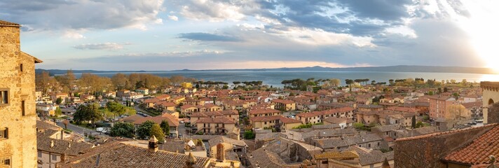 Panoramic aerial view of the old famous city of Bolsena and Lake Bolsena at sunset. Province of Viterbo, Italy, Lazio. Cityscape and tiled roofs - obrazy, fototapety, plakaty