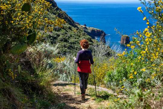 Sizilien im Frühling: Küstenwanderung Insel Lipari - Frau mit Stöcken wandert im Südwesten in Blütenpracht