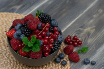 Ripe sweet different berries in bowl on wooden table. Harvest Concept.