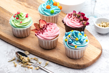 Colorful cupcakes with different modern decoration on wooden board with spoon and ingredients on blue background