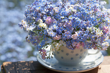 Spring bouquet of forget-me-nots flowers in a cup on the table, blurred background of a flower bed...