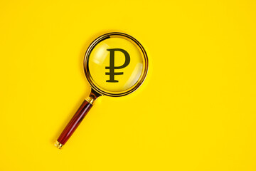 Ruble symbol under magnifying glass, on yellow background.