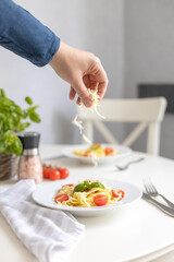 Girl's hands adding, sprinkles grated cheese to Italian homemade pasta with cherry tomatoes. Serving the dish. vertical photo