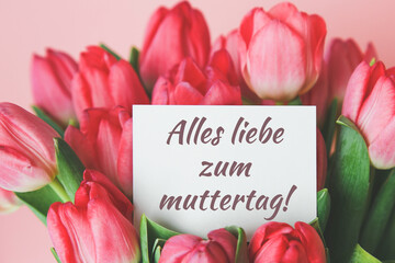 white gift card with the inscription happy mother s day in german in a bouquet of beautiful tulips,...