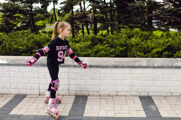 Girl child rollerblading in fall protection in the park. The child actively spends his free time, enthusiastically rollerblading. A girl in sportswear is engaged in roller skating. Free space for text