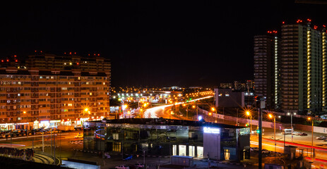 Fototapeta na wymiar Night city lights. Crossroads with passing cars, lanterns and tall houses, long exposure. Panorama
