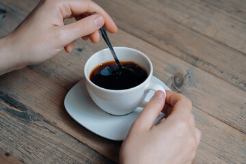 Close up of man enjoying in cup of morning coffee and mixing it with a spoon.