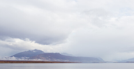 Fototapeta premium montañas y colinas en la distancia con mar y nubes nimbostratos blancos y plomos paisaje costanero nublado panorámico 