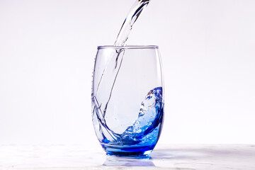 Pouring purified drinking water into a blue glass, white background carrara marble base. empty glass.