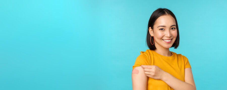 Vaccine Campaign From Covid-19. Young Beautiful, Healthy Asian Woman Showing Shoulder With Bandaid, Concept Of Vaccination, Standing Over Blue Background