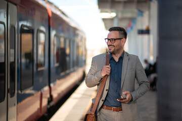 Young businessman using mobile phone at train station and text messaging.