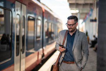 Businessman using mobile phone at train station - obrazy, fototapety, plakaty
