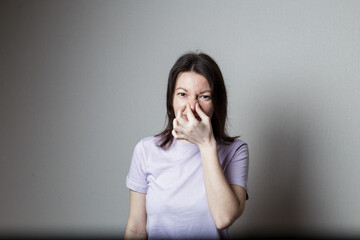 Portrait of a frustrated woman pinch her nose with disgust on her face because of a bad smell on a gray background - obrazy, fototapety, plakaty