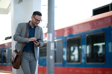 Man using phone at railroad station while waitining for train