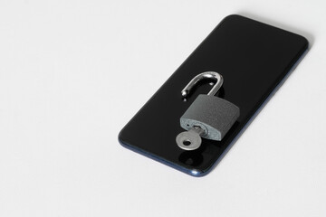 Modern mobile phone and open padlock with key on white background. Concept of cracking password on smartphone. Problem of protecting digital information. Copy space. White background.