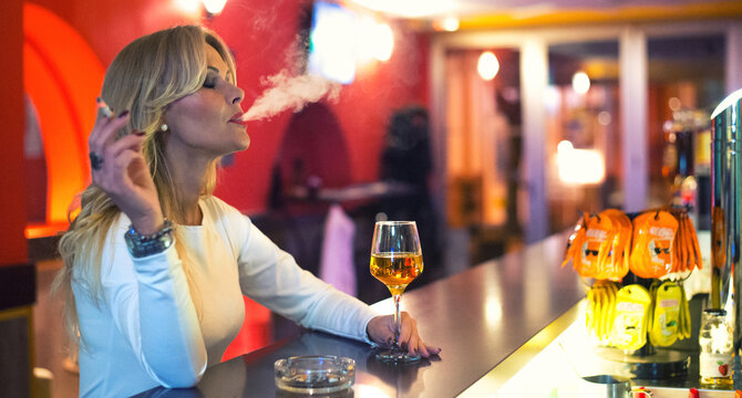 Lonely woman drinking and smoking cigarettes in the bar at night