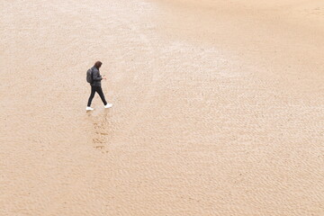 In their own world... A young male walks across an isolated beach, staring at the smartphone in his...