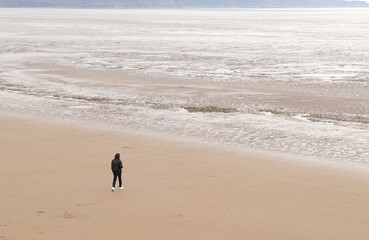 Lone figure on Weston-super-Mare beach, smartphone in hand, walking out to a sea of mud