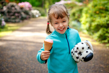 Adorable little girl eating tasty fresh ice cream and holding dog toy - 502481842