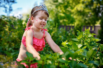 Adorable cute little caucasian four year old kid girl wearing swimming suit and princess tiara enjoying time in her home garden - 502481843
