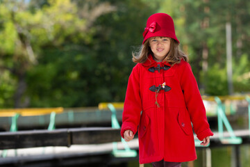Cute happy little girl wearing red retro hat and coat posing in city park - 502481863