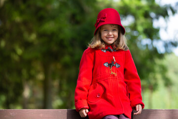 Cute happy little girl wearing red retro hat and coat posing in city park - 502481869
