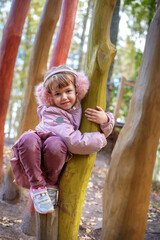 Cute happy little girl in winter faux fur ear muffs plays outdoors at wooden playground on warm sunny autumn day - 502481882