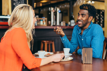 black man drinking coffee and eating chocolate with a Caucasian woman in a restaurant