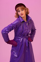 Young pretty girl in fashionable retro-style clothes, violet headband amd raincoat and gloves. Violet background. Beautiful lighting, unusual portrait